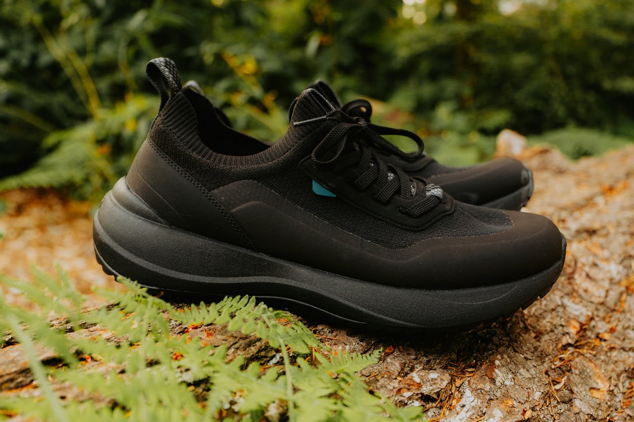 Fashionable black sneakers placed on a log in an autumn forest setting, showcasing outdoor style and comfort.