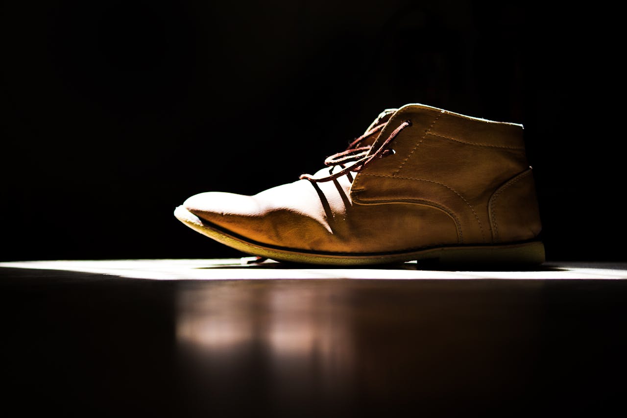 Side view of a leather chukka boot spotlighted on a dark background in a studio setting.